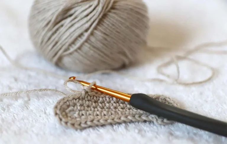 En virkning ligger på en filt med en virknål och ett sandfärgat garnnystan fäst vid arbetet