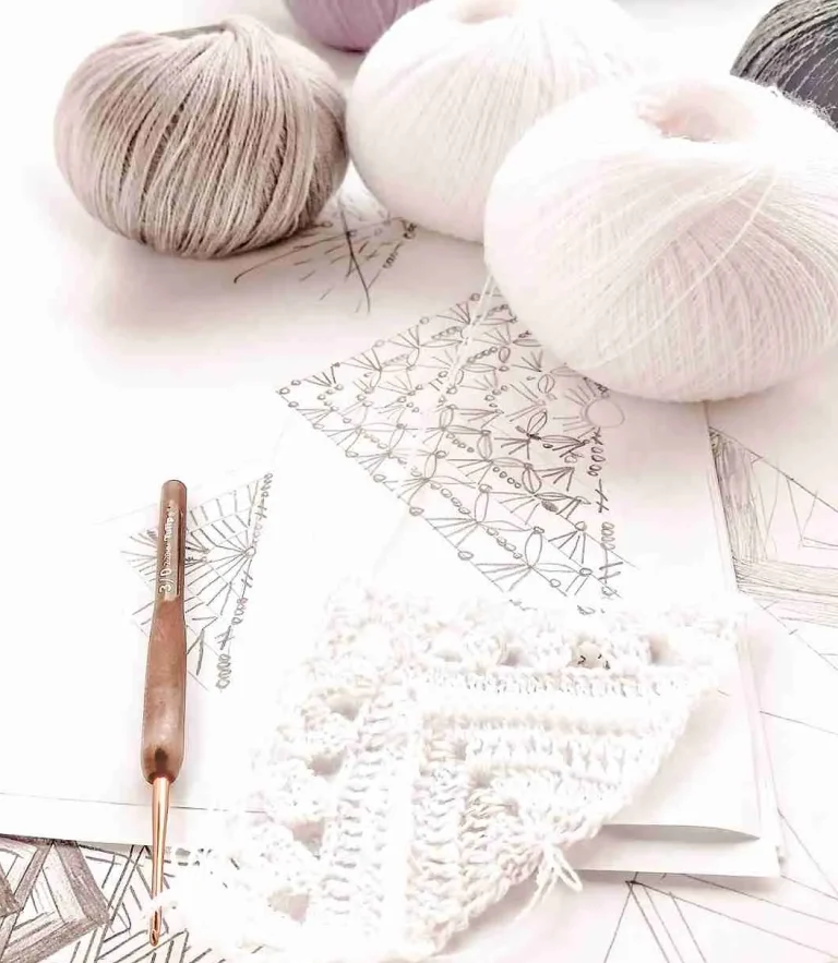 Tre garnnystan liggandes på ett virkmönster för en sjal med en virknål bredvid.